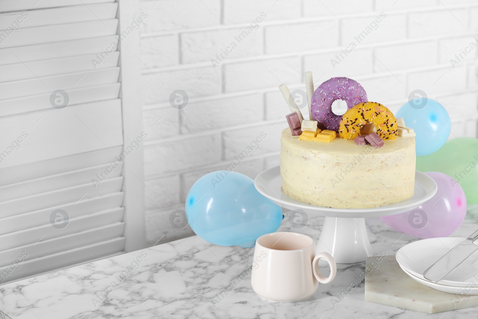 Photo of Delicious cake decorated with sweets, tableware and balloons on white marble table, space for text