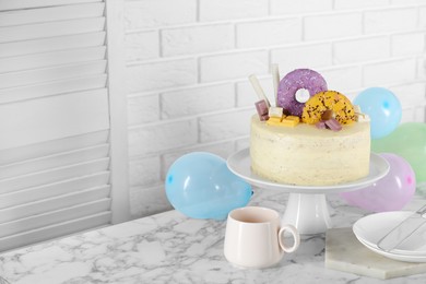 Photo of Delicious cake decorated with sweets, tableware and balloons on white marble table, space for text