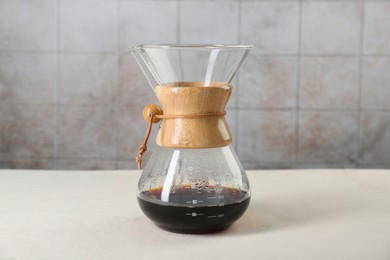 Photo of Glass chemex coffeemaker with tasty drip coffee on white table