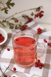 Cup with hawthorn tea and berries on table