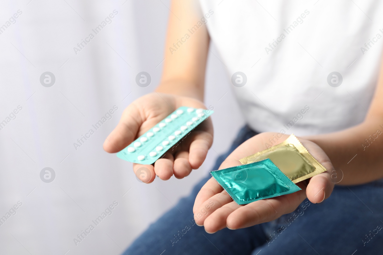 Photo of Young woman holding birth control pills and condoms on light background, closeup. Safe sex concept