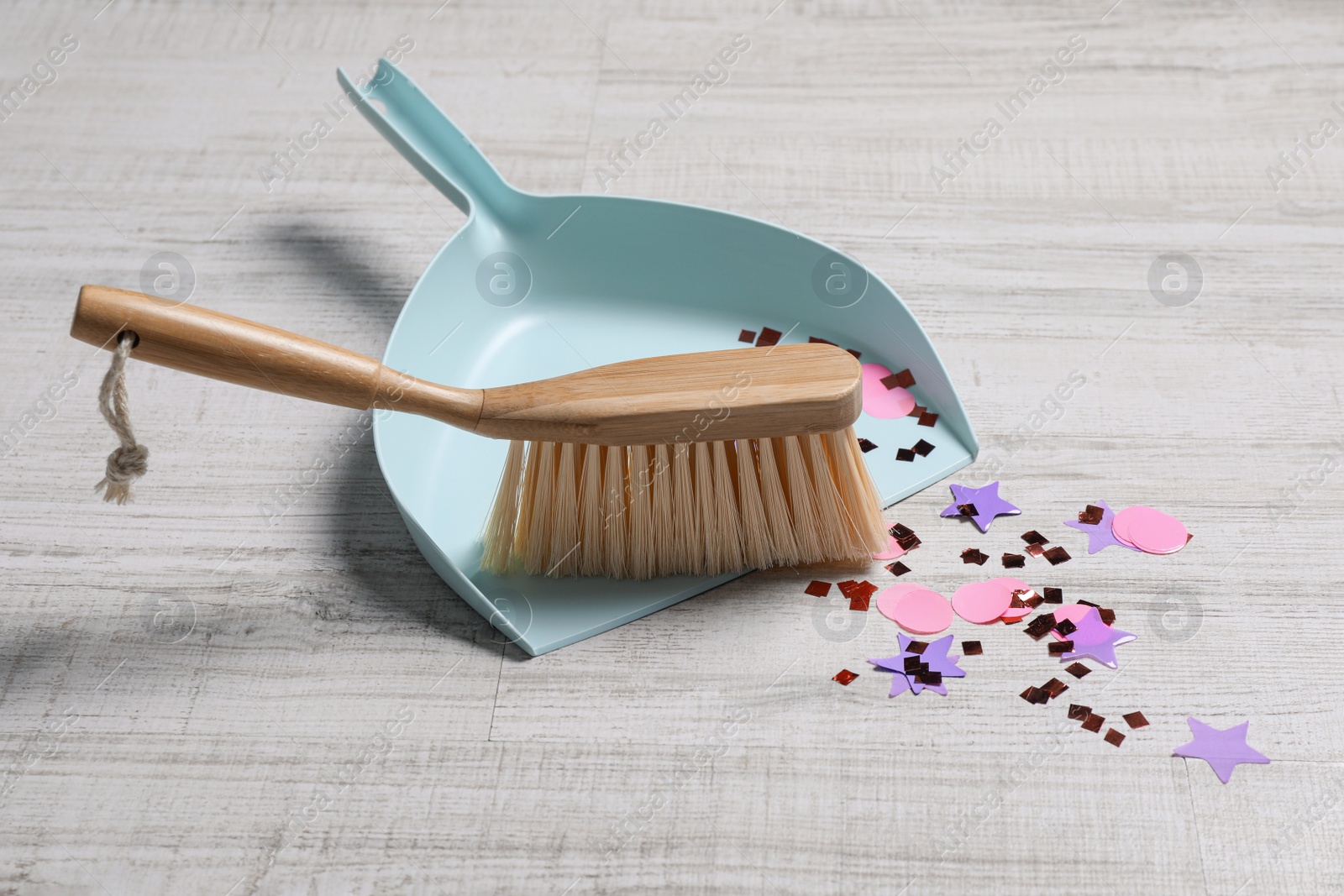 Photo of Light blue dustpan, wooden brush and bright confetti on floor