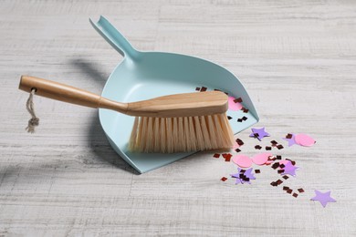 Photo of Light blue dustpan, wooden brush and bright confetti on floor