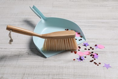 Light blue dustpan, wooden brush and bright confetti on floor