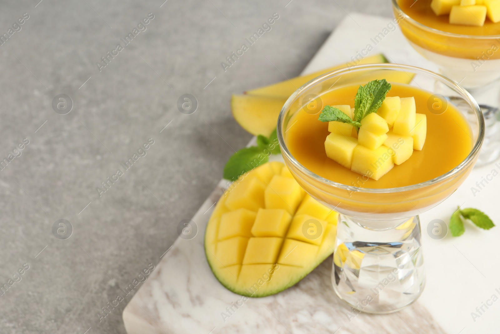 Photo of Delicious panna cotta with mango coulis and fresh fruit pieces on light grey table. Space for text