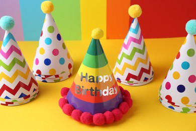 Different bright party hats with pompoms on color background