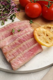 Pieces of delicious tuna steak with microgreens, tomatoes and lemon on table, closeup