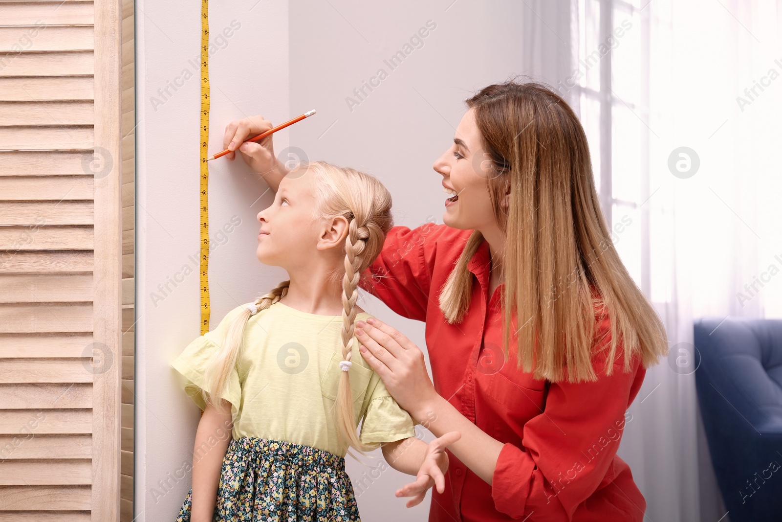 Photo of Young woman measuring her daughter's height at home