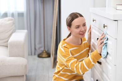 Photo of Woman cleaning chest of drawers with rag at home