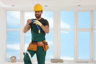 Photo of Electrician with insulating tape standing on ladder indoors. Space for text