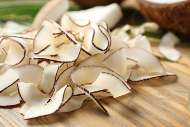 Photo of Pile of tasty coconut chips on wooden board, closeup