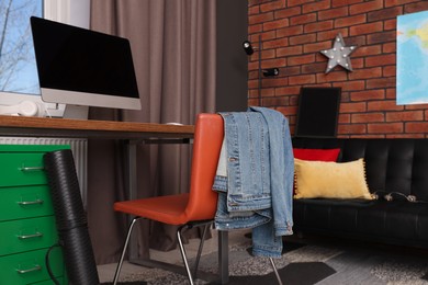 Stylish teenager's room with computer and black sofa near brick wall