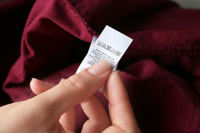 Photo of Woman reading clothing label with care instructions on red garment, closeup