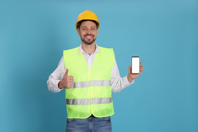 Photo of Male industrial engineer in uniform with phone on light blue background