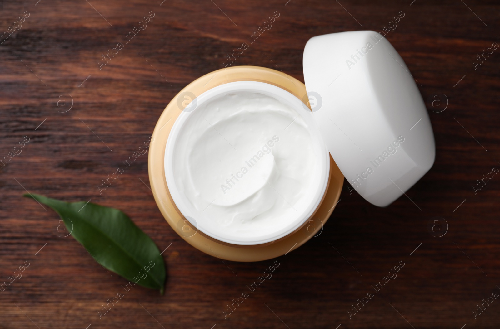 Photo of Jar of face cream and green leaf on wooden table, top view