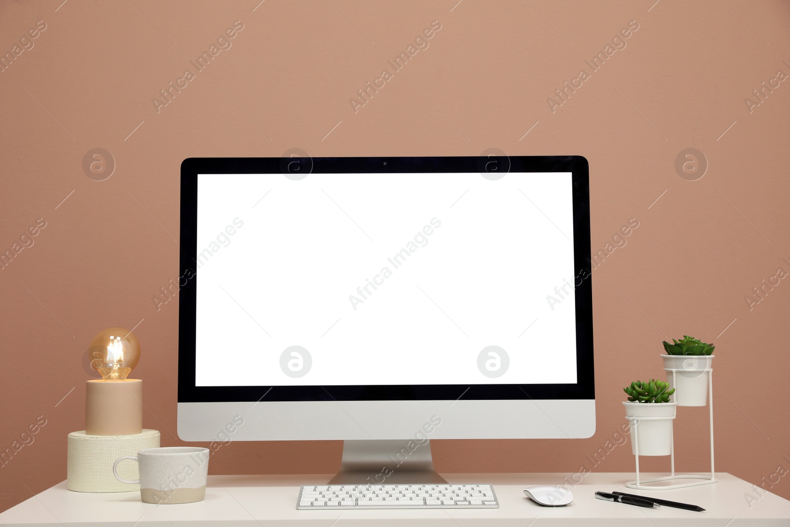 Photo of Comfortable workplace with blank computer display on desk near light brown wall. Space for text