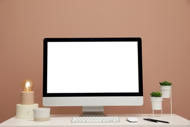 Photo of Comfortable workplace with blank computer display on desk near light brown wall. Space for text