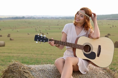Photo of Beautiful hippie woman with guitar on hay bale in field, space for text