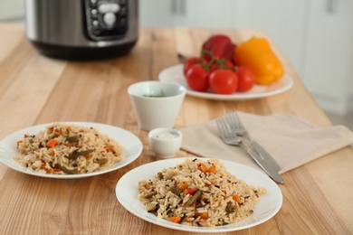 Delicious rice with vegetables and multi cooker on wooden table