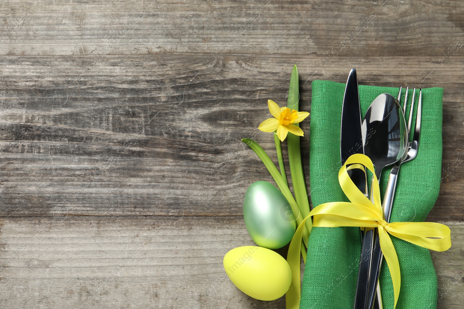 Photo of Cutlery set, painted eggs and beautiful flower on wooden table, flat lay with space for text. Easter celebration