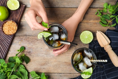 Woman decorating freshly made cocktail with mint at wooden table, top view