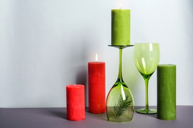 Photo of Decorative wax candles and wineglasses on table against light background