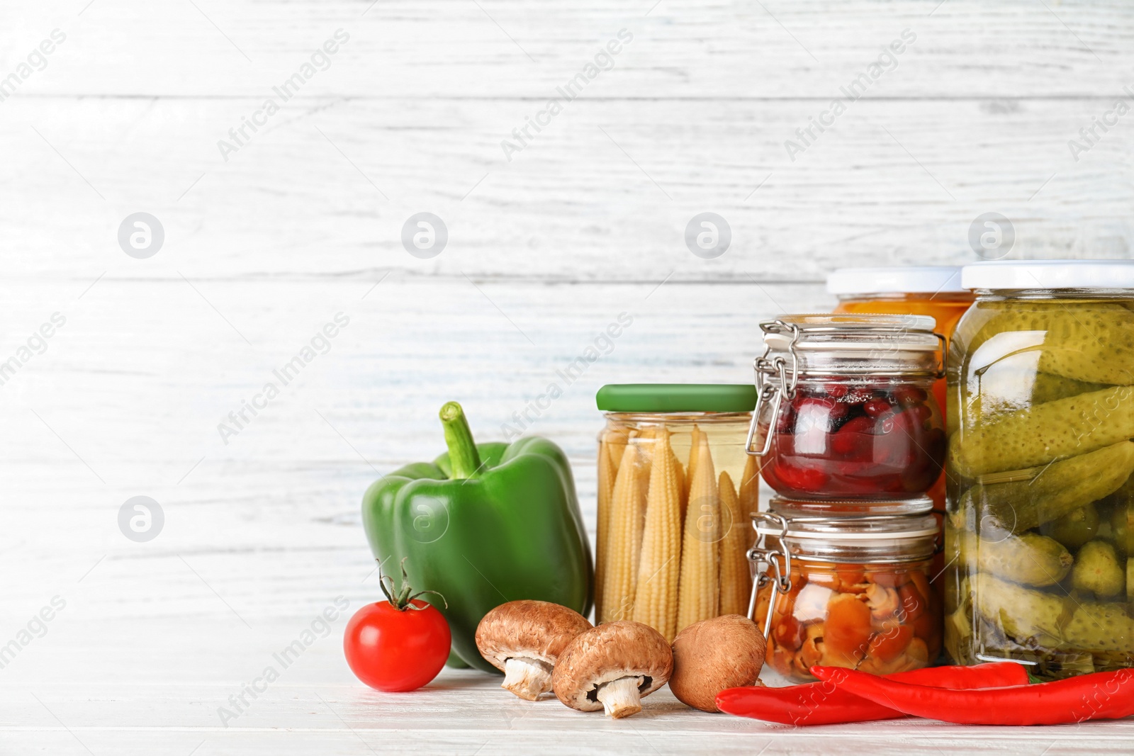 Photo of Glass jars with different pickled vegetables on white wooden table. Space for text