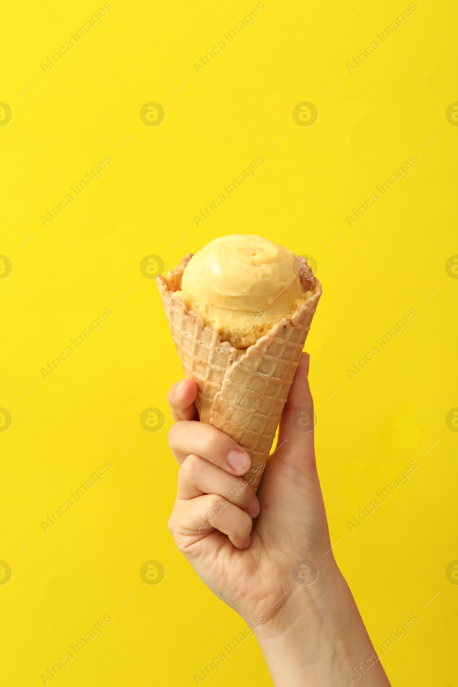 Photo of Woman holding waffle cone with delicious ice cream on yellow background, closeup