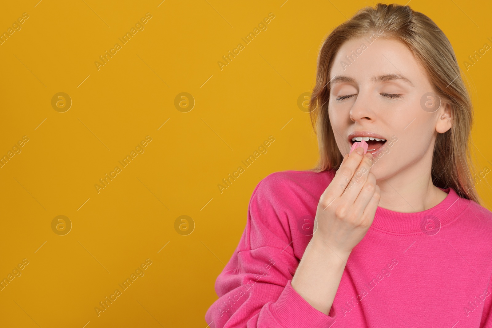 Photo of Woman putting bubble gum into mouth on yellow background. Space for text