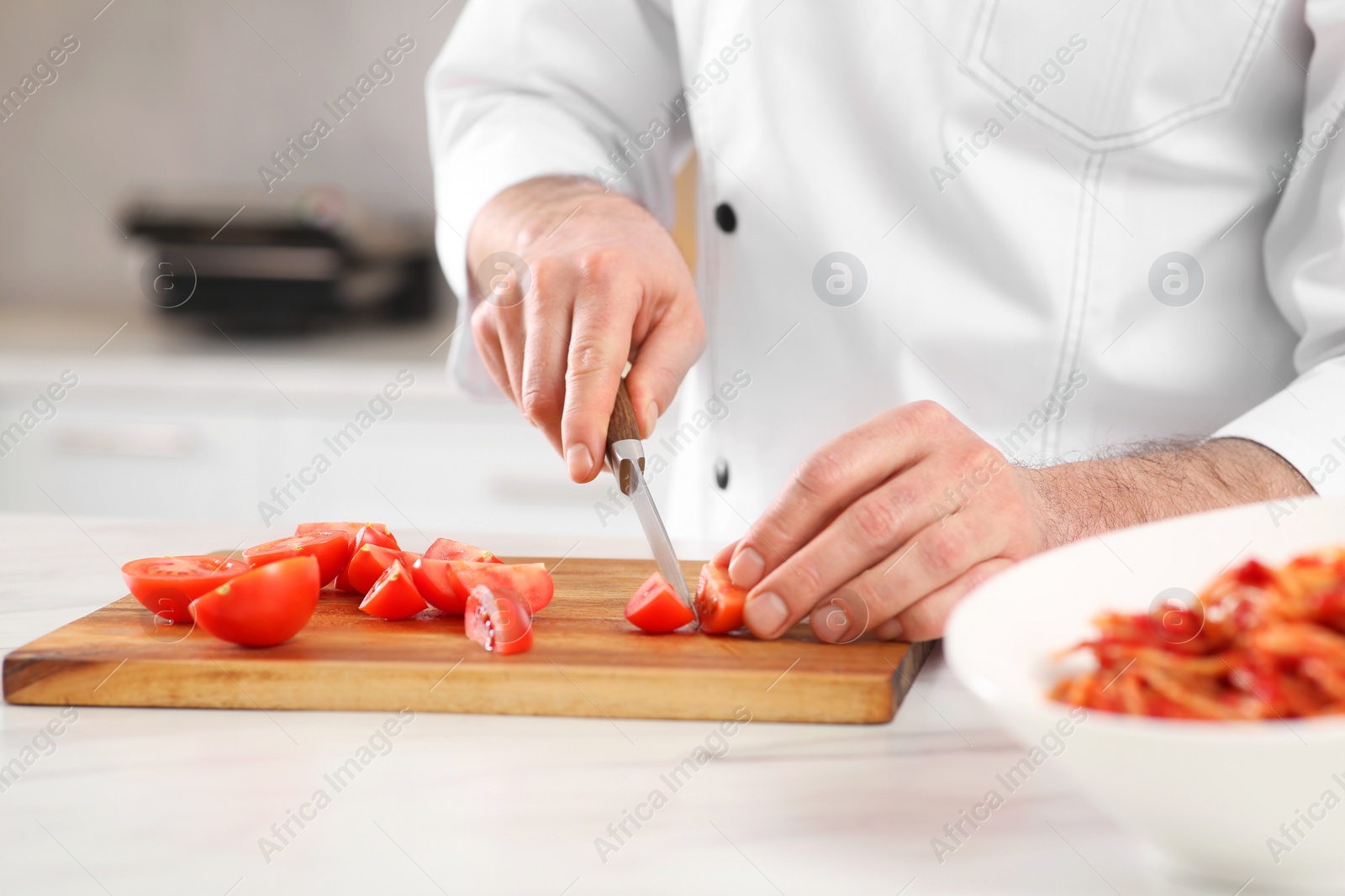 Photo of Chef cutting tomatoes at marble table in kitchen, closeup