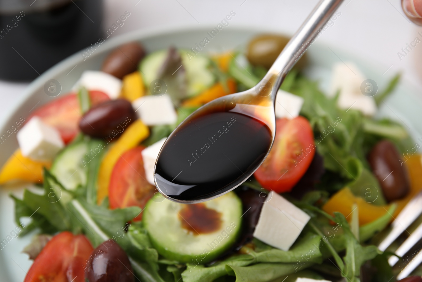 Photo of Pouring vinegar from spoon into plate with salad at table, closeup