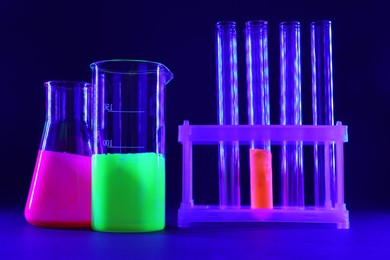 Photo of Laboratory glassware with luminous liquids on dark blue background