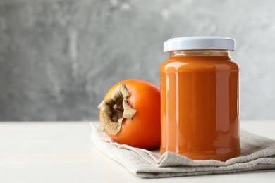 Delicious persimmon jam in glass jar and fresh fruit on white wooden table, space for text