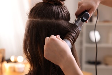 Photo of Hairdresser using curling hair iron while working with woman in salon, closeup
