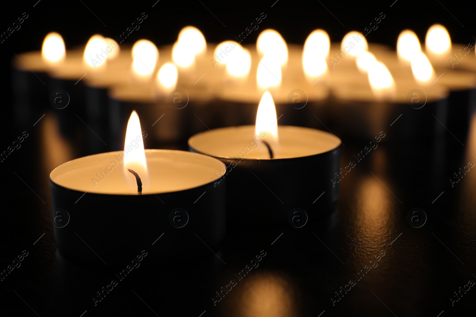 Photo of Burning candles on table in darkness, closeup. Funeral symbol