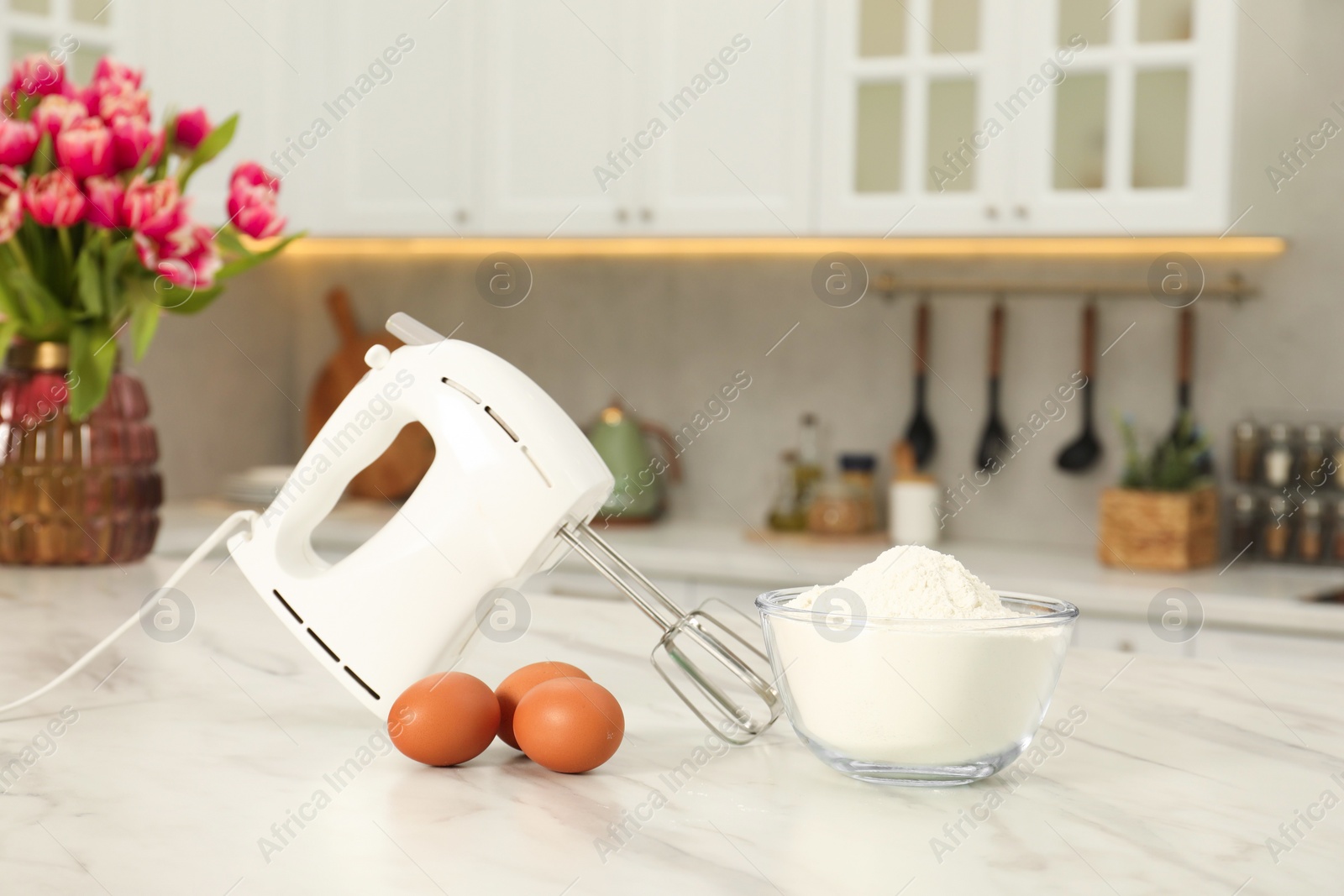 Photo of Modern mixer, eggs and bowl with flour on white marble table in kitchen