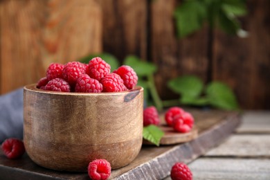 Photo of Bowl of fresh ripe raspberries on wooden table, space for text