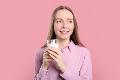 Photo of Smiling woman with milk mustache holding glass of tasty dairy drink on pink background