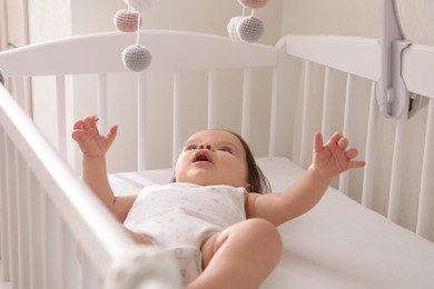 Cute little baby looking at hanging mobile in crib