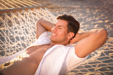 Man relaxing in hammock on beach at sunset