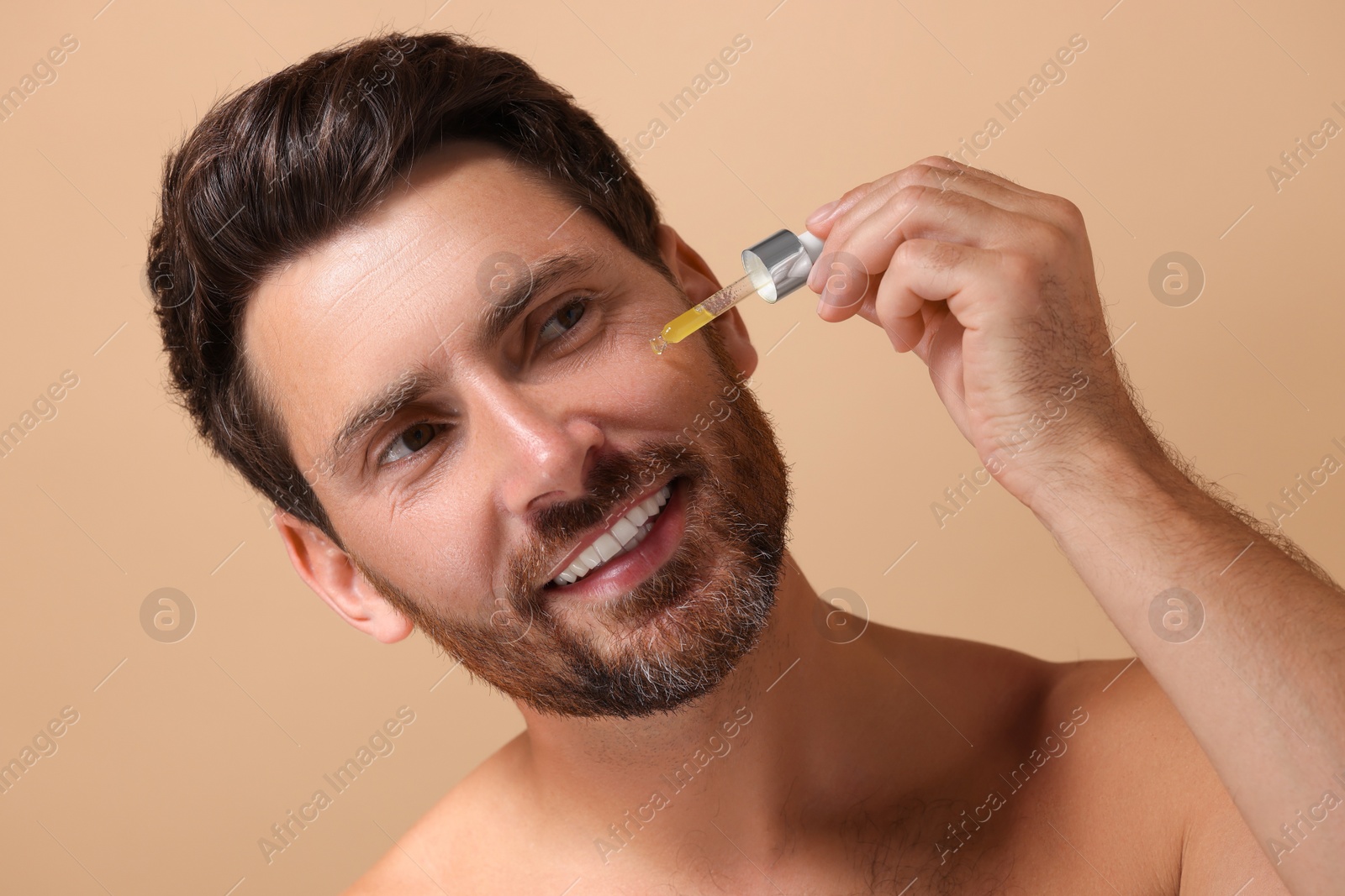 Photo of Smiling man applying cosmetic serum onto his face on beige background, closeup