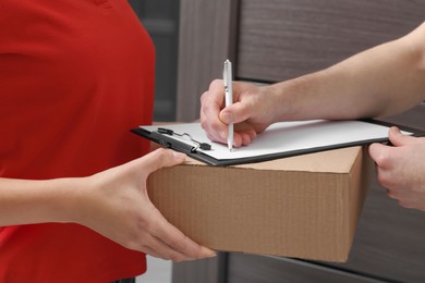 Photo of Man signing for delivered parcel from courier indoors, closeup