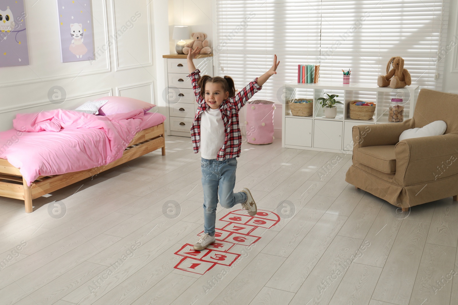 Photo of Cute little girl playing hopscotch at home