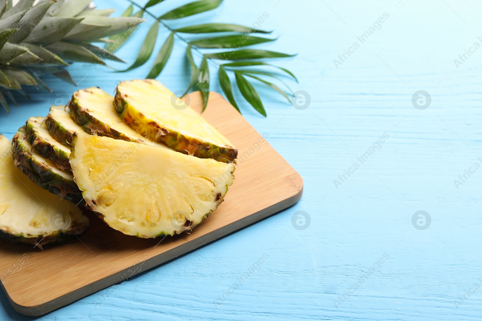 Photo of Slices of ripe juicy pineapple and green leaf on light blue wooden table. Space for text