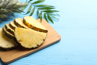 Slices of ripe juicy pineapple and green leaf on light blue wooden table. Space for text