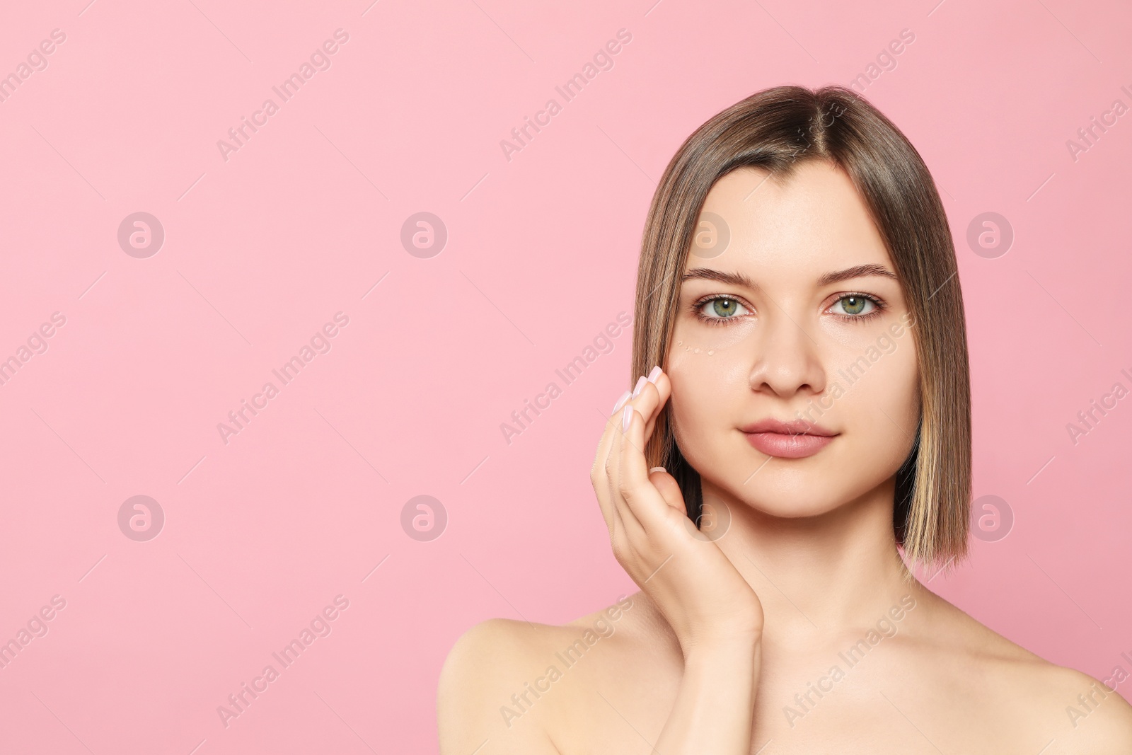 Photo of Young woman with cream around eye on pink background, space for text