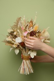 Woman holding beautiful dried flower bouquet on green background, closeup