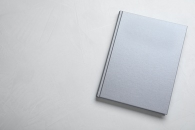 Photo of Closed grey book with hard cover on light grey table, top view. Space for text