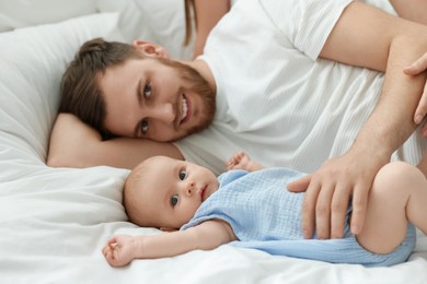 Photo of Father with his cute baby on bed indoors