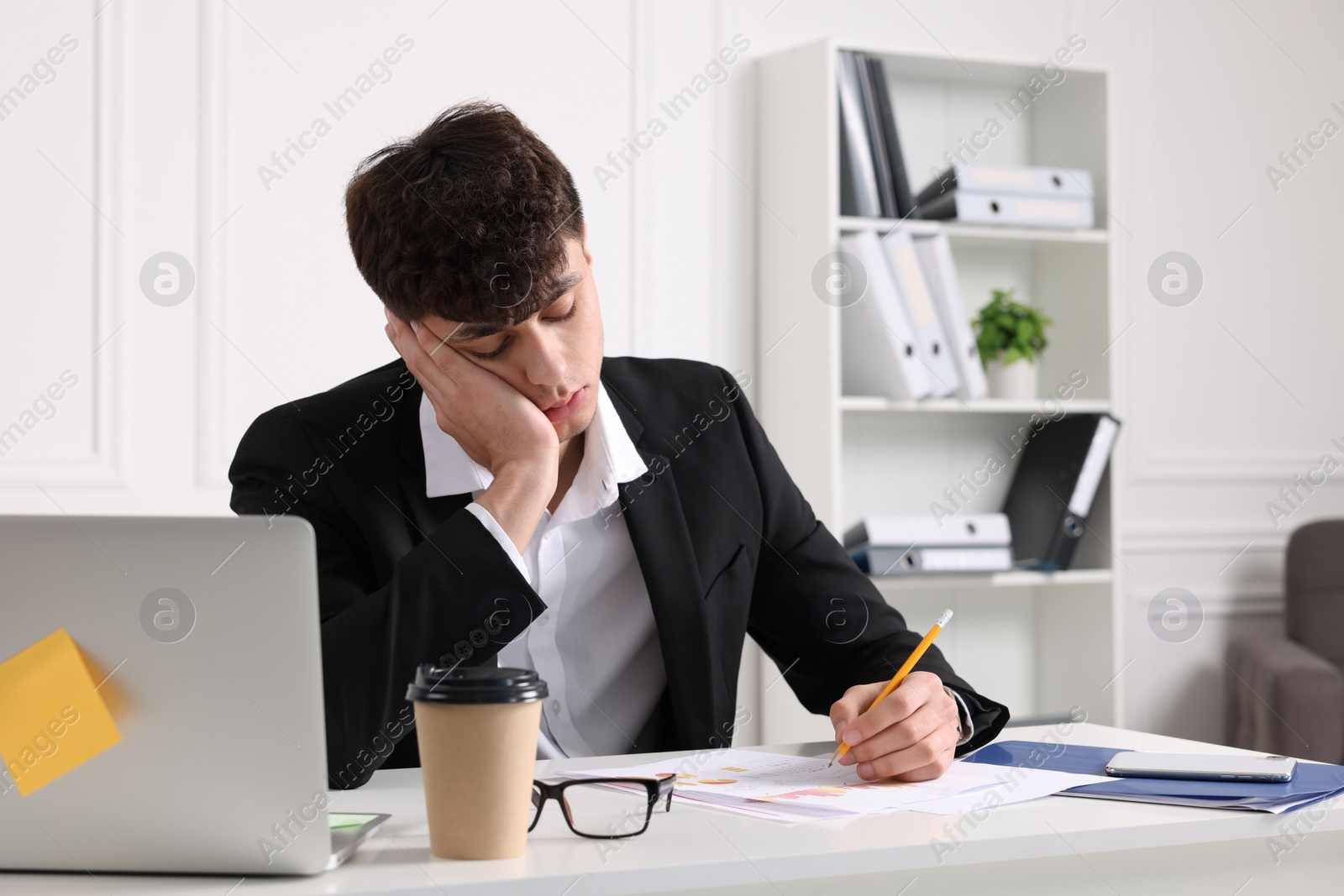 Photo of Tired young man working at table in office. Deadline concept